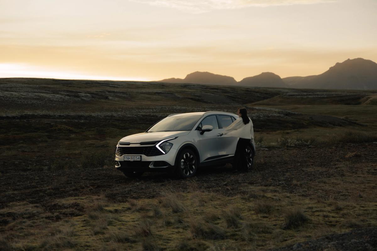 Kia Sportage sjálfkeyrslubíll á Íslandi, jeppi sem stendur í opnu hálendislandslagi með manneskju við hliðina