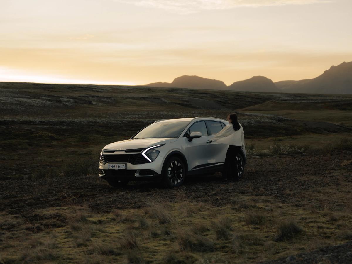 Sportage Highland landslag Kia Sportage sjálfkeyrslubíll á Íslandi, jeppi sem stendur í opnu hálendislandslagi með manneskju við hliðina