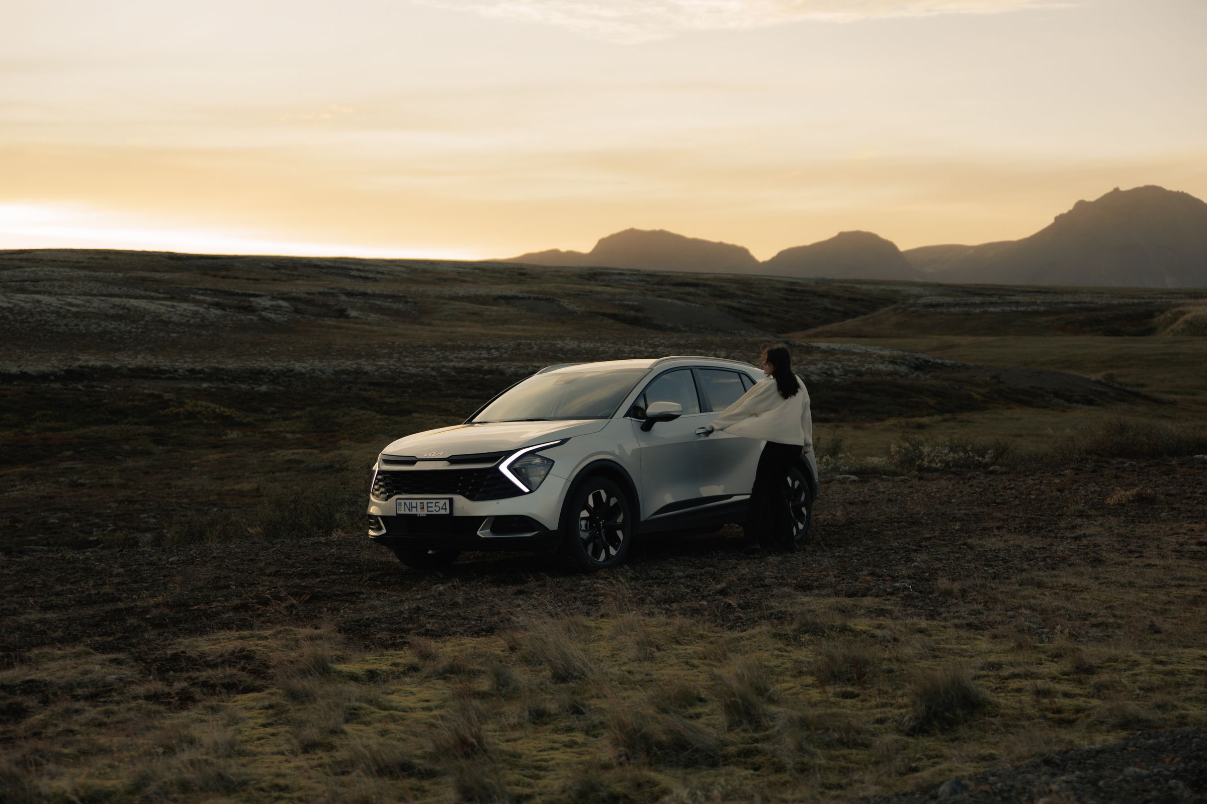 Sportage Highland landslag Kia Sportage sjálfkeyrslubíll á Íslandi, jeppi sem stendur í opnu hálendislandslagi með manneskju við hliðina