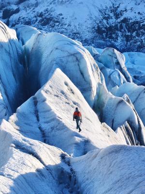 a man in a red jacket is walking on top of a large iceberg .