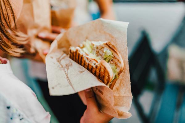 a person is holding a sandwich wrapped in brown paper .