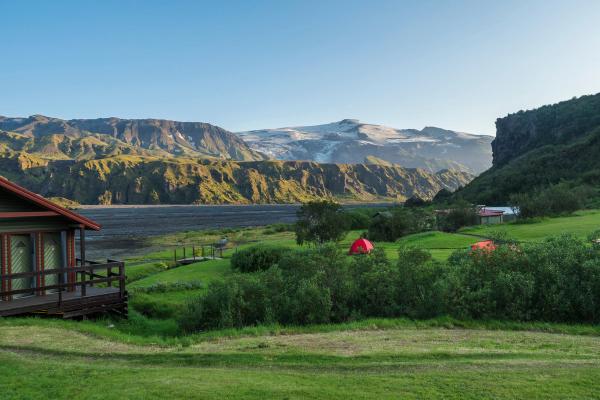 une petite maison avec une tente rouge au milieu d'un champ avec des montagnes en arrière-plan .