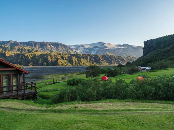 a small house with a red tent in the middle of a field with mountains in the background .