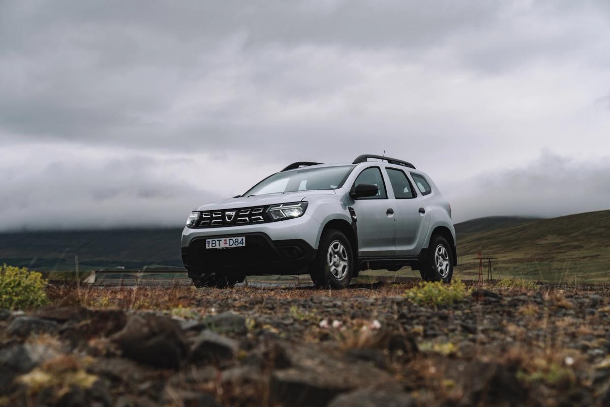 Dacia Duster SUV rental Iceland parked on rocky ground overlooking open highland landscape