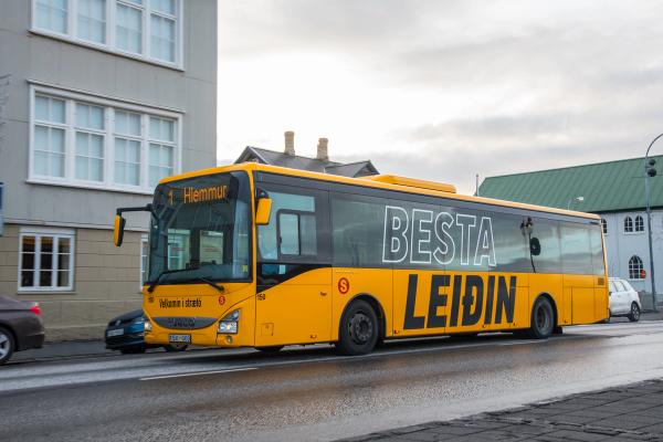 a yellow bus is driving down a street in front of a building .