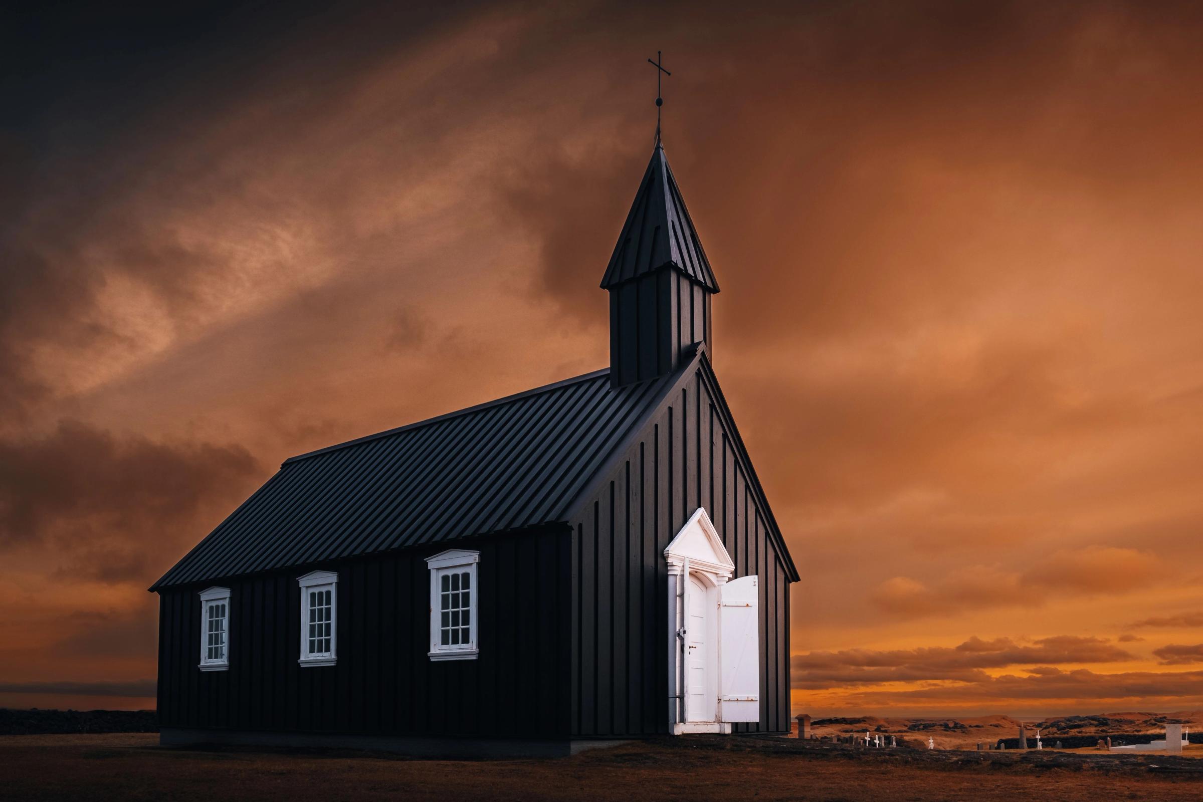 Black church with white trim and open doors under a dramatic orange and dark sky.