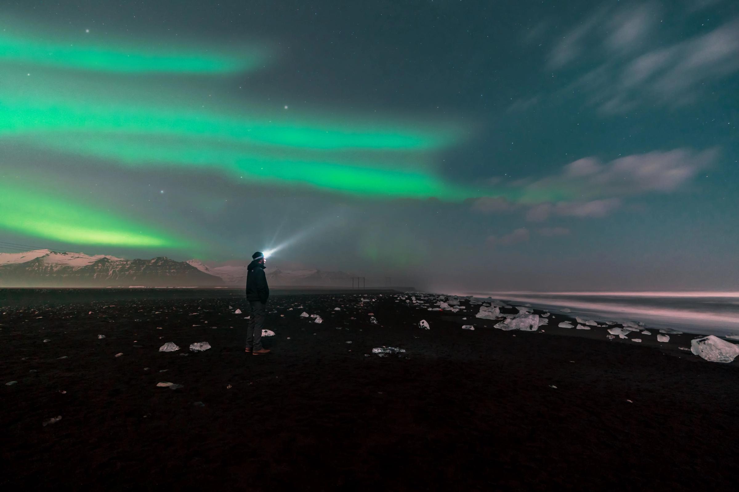Hombre en Diamond Beach bajo la aurora boreal