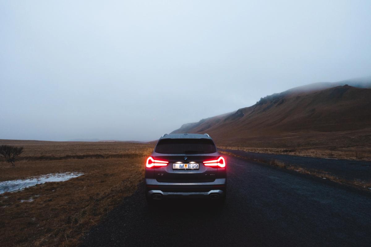 BMW X3 rear view with illuminated taillights on open highland landscape road