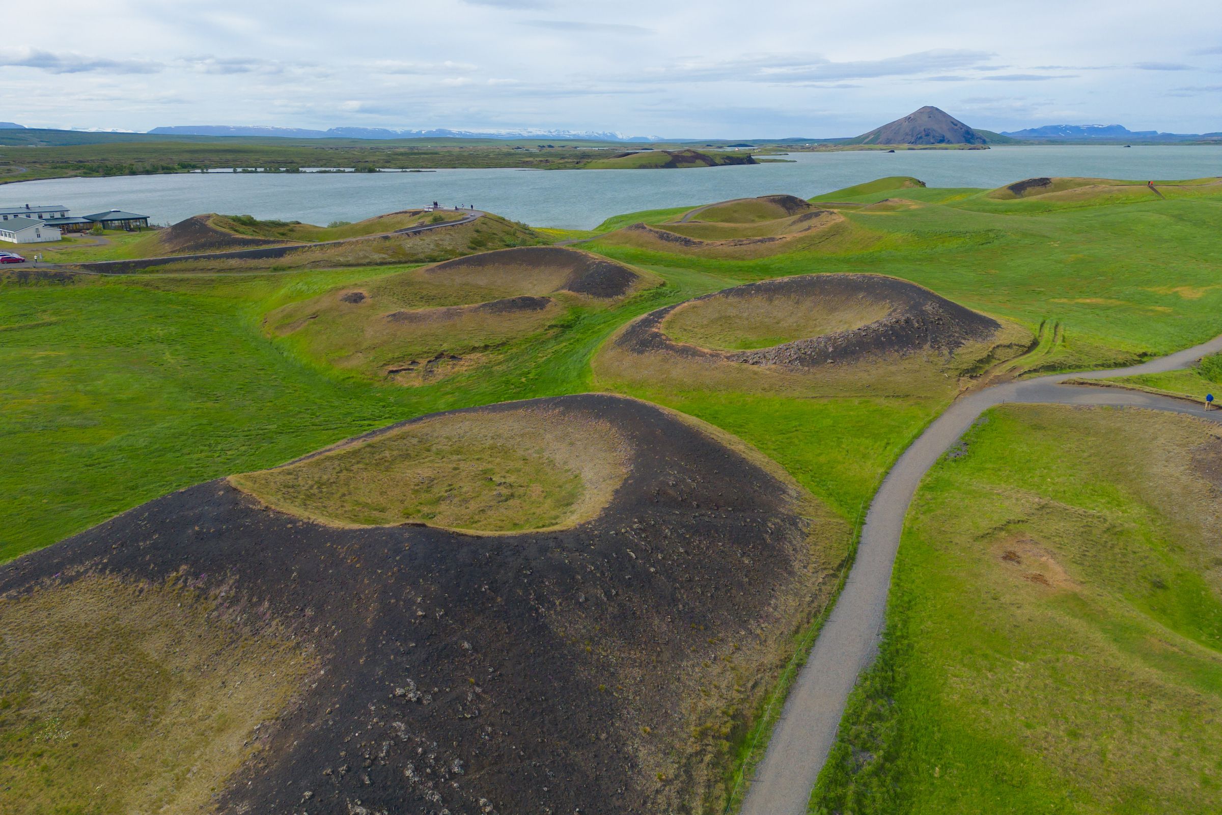 an aerial view of a volacanos with a lake in the background at skútustaðagígar by mývatn in iceland.