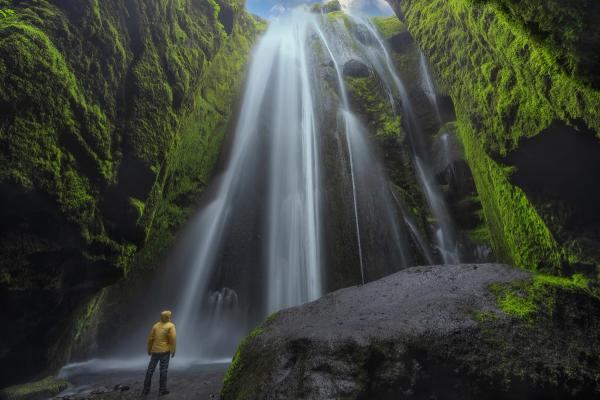 a man in a yellow jacket is standing in front of a waterfall .