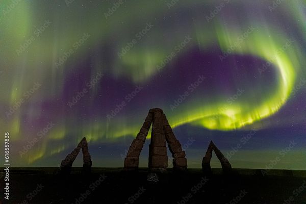 El Arctic Henge recortado contra una brillante aurora boreal verde y púrpura.