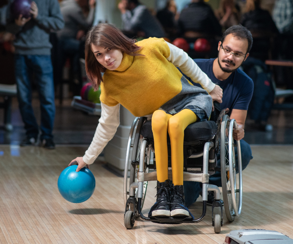 Rullestolbruker spiller bowling med assistent