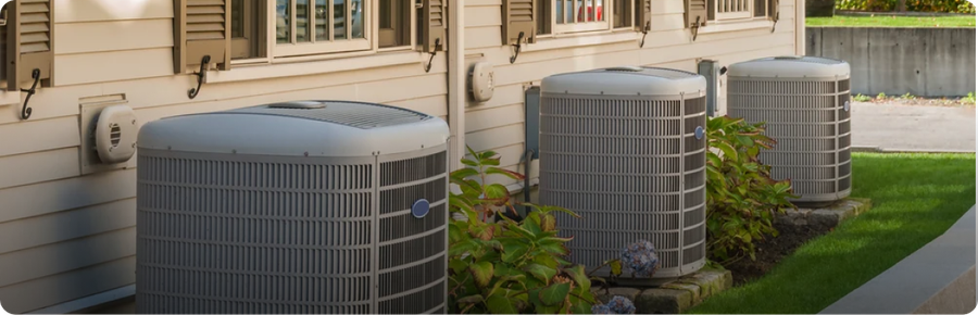 Three residential AC condenser units beside a house