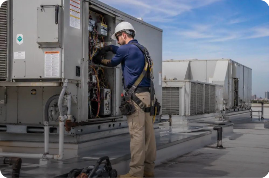 Technician in a hard hat servicing a commercial rooftop AC unit