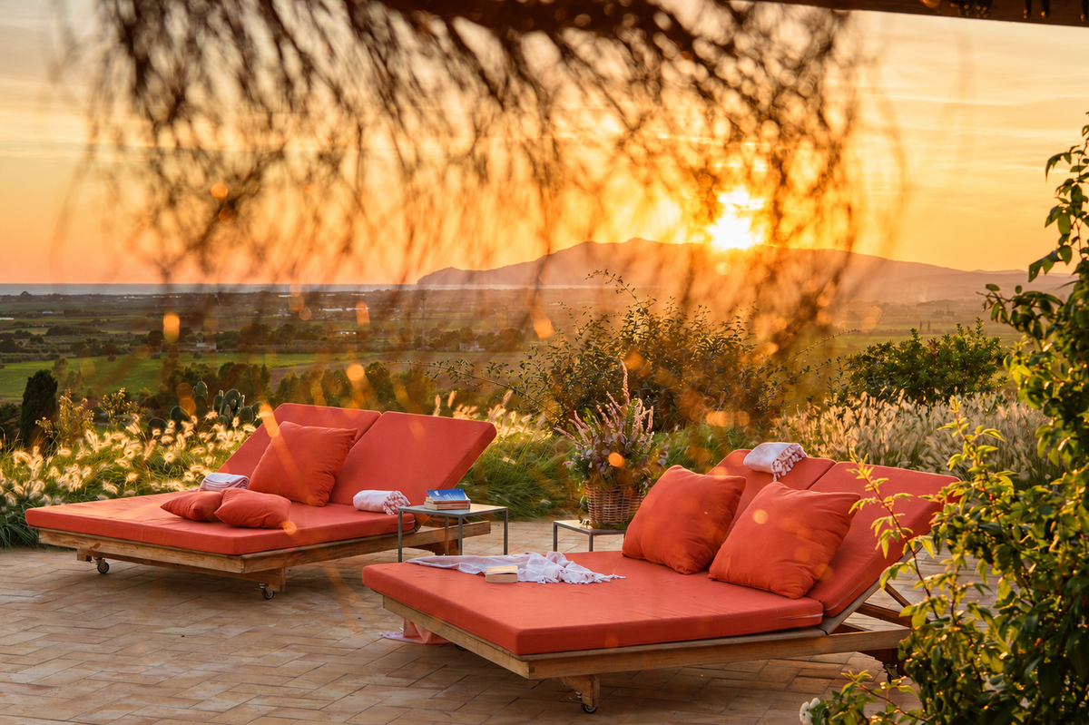 Orange loungers on the terrace at sunset, with a headland on the horizon