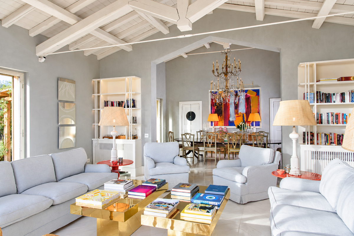 Living room with pale sofas, gilded tables and bookshelves, the dining room beyond