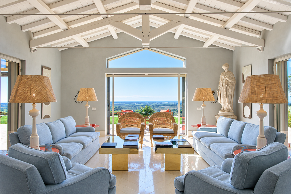 Living room under white beams, with blue sofas and a glass door onto the view
