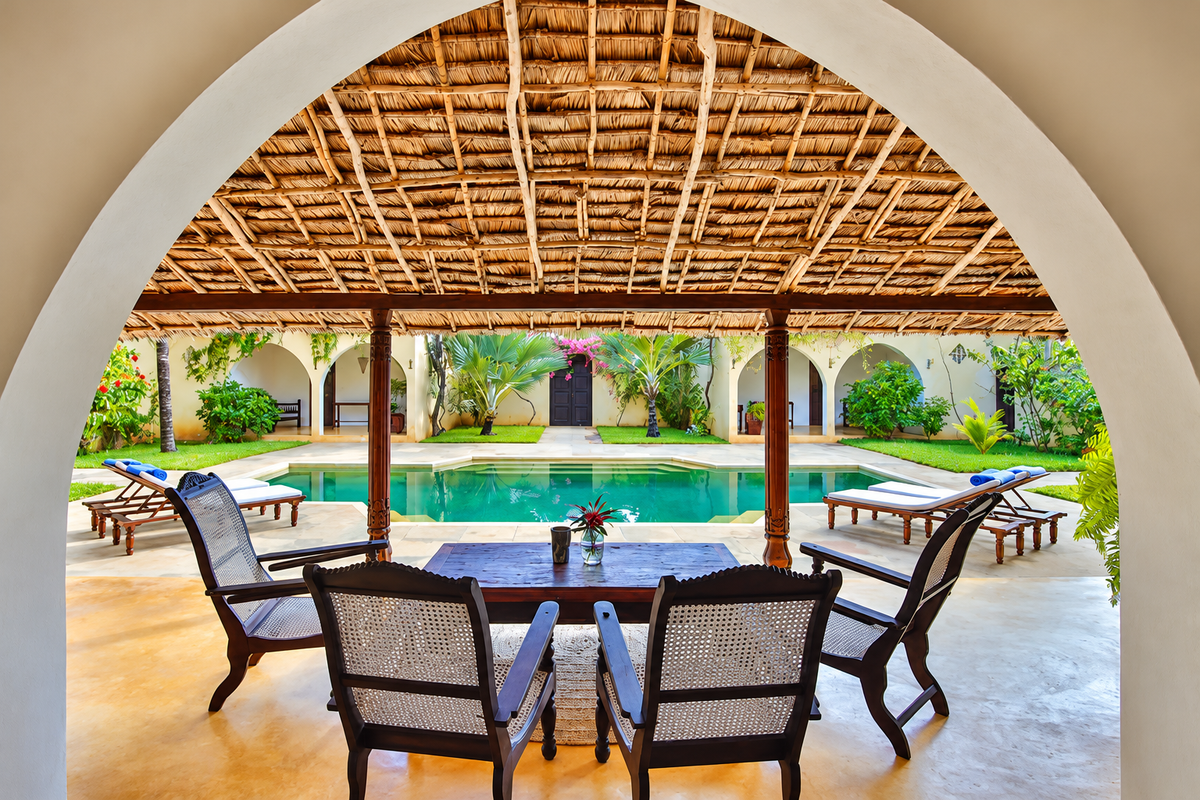 Poolside dining under a thatched roof framed by an arch