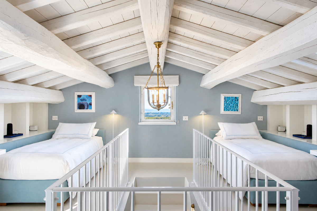 Two single beds under white beams, either side of a stair rail