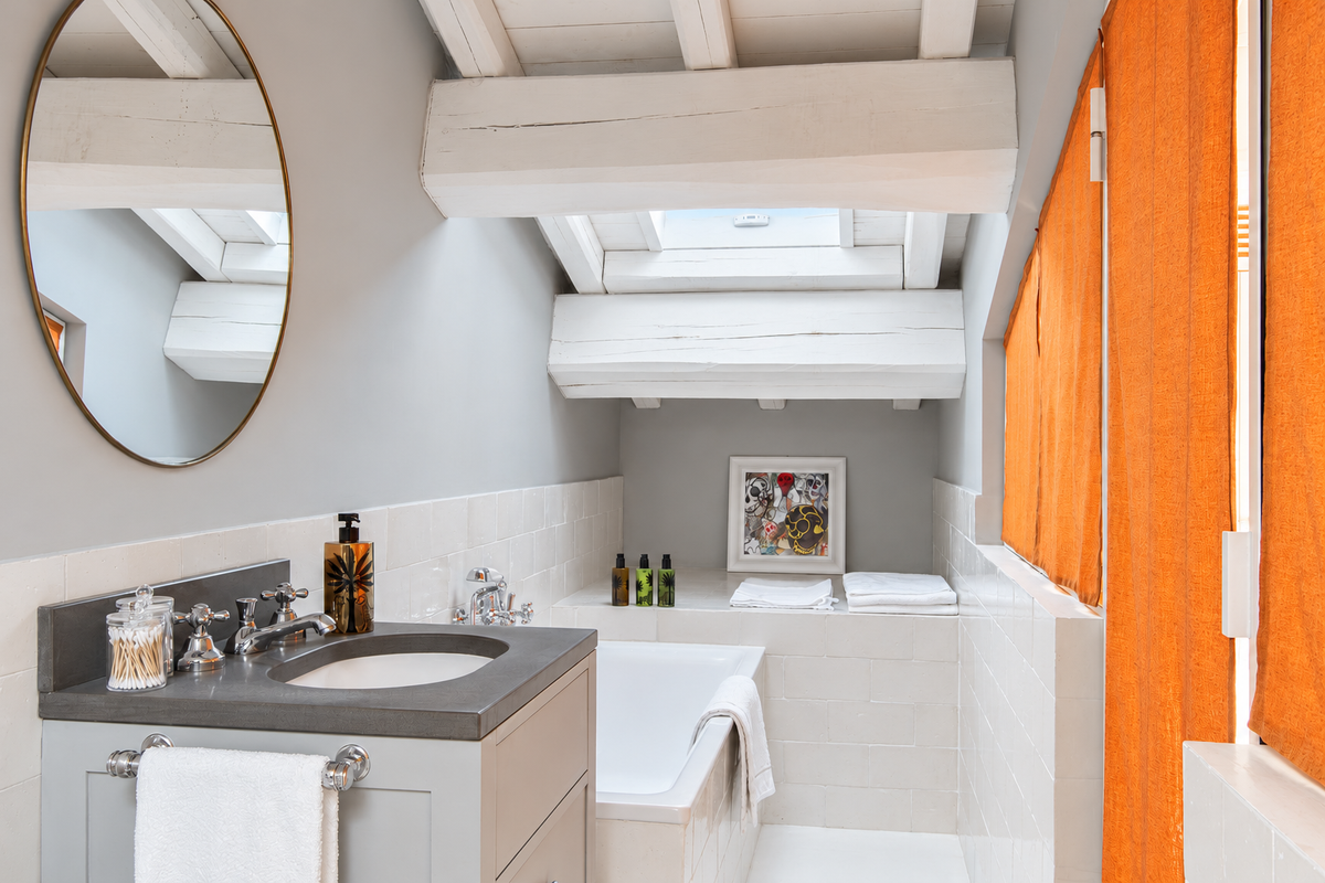 Bathroom under the roof with a bathtub and orange curtains