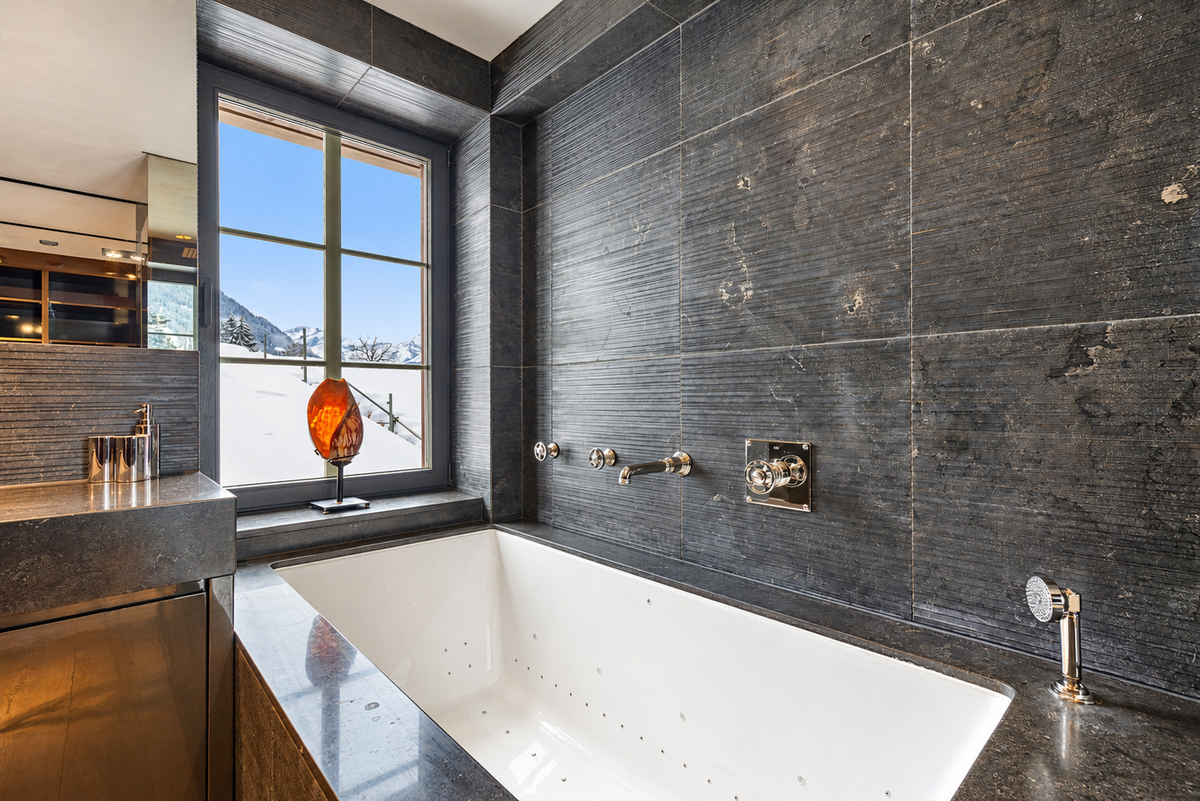 Jacuzzi bath in dark stone beside a window onto the mountains