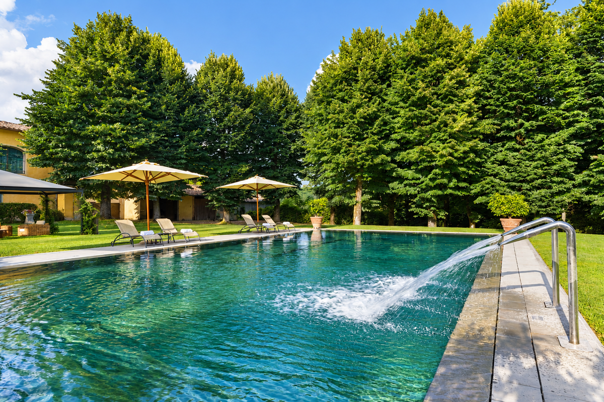 Castello del Monsignore's stone pool with a fountain jet and parasols among tall trees