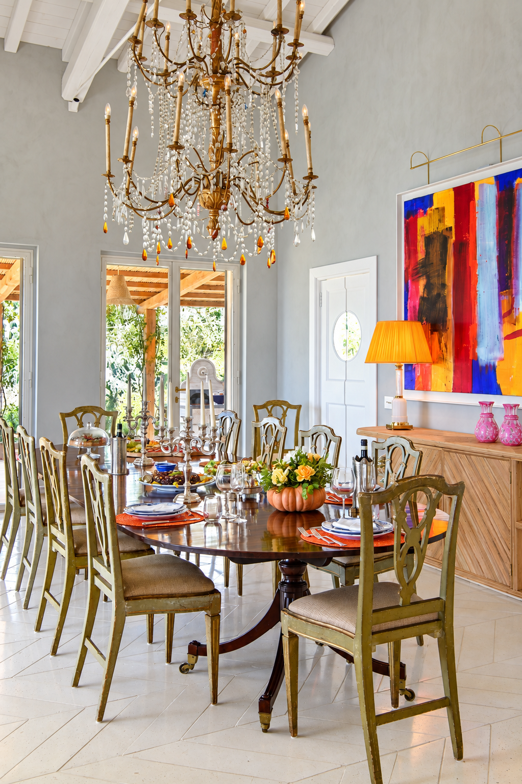 Dining table laid beneath a crystal chandelier, with an abstract painting