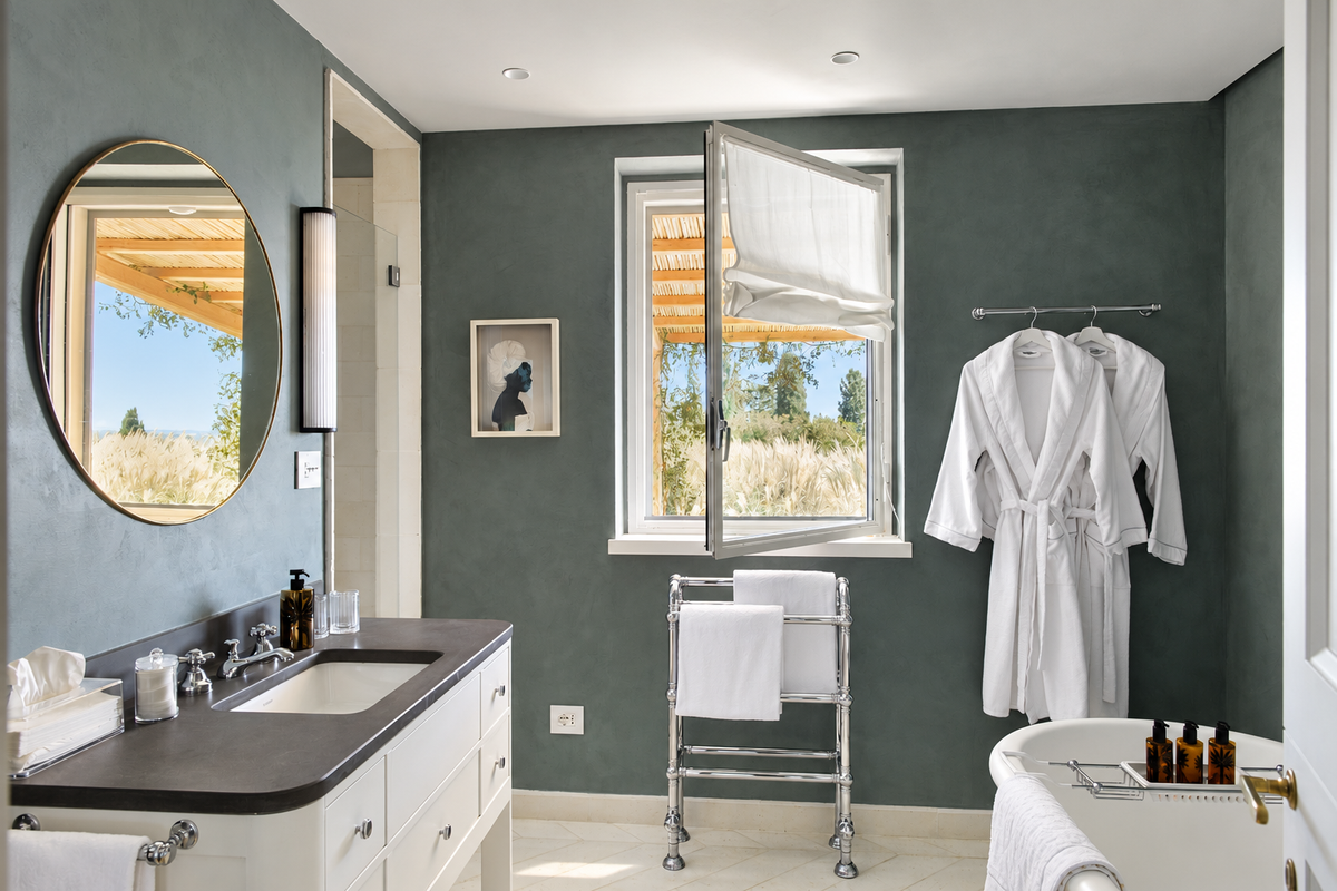 Bathroom with a round mirror, a bathtub and a window onto the garden