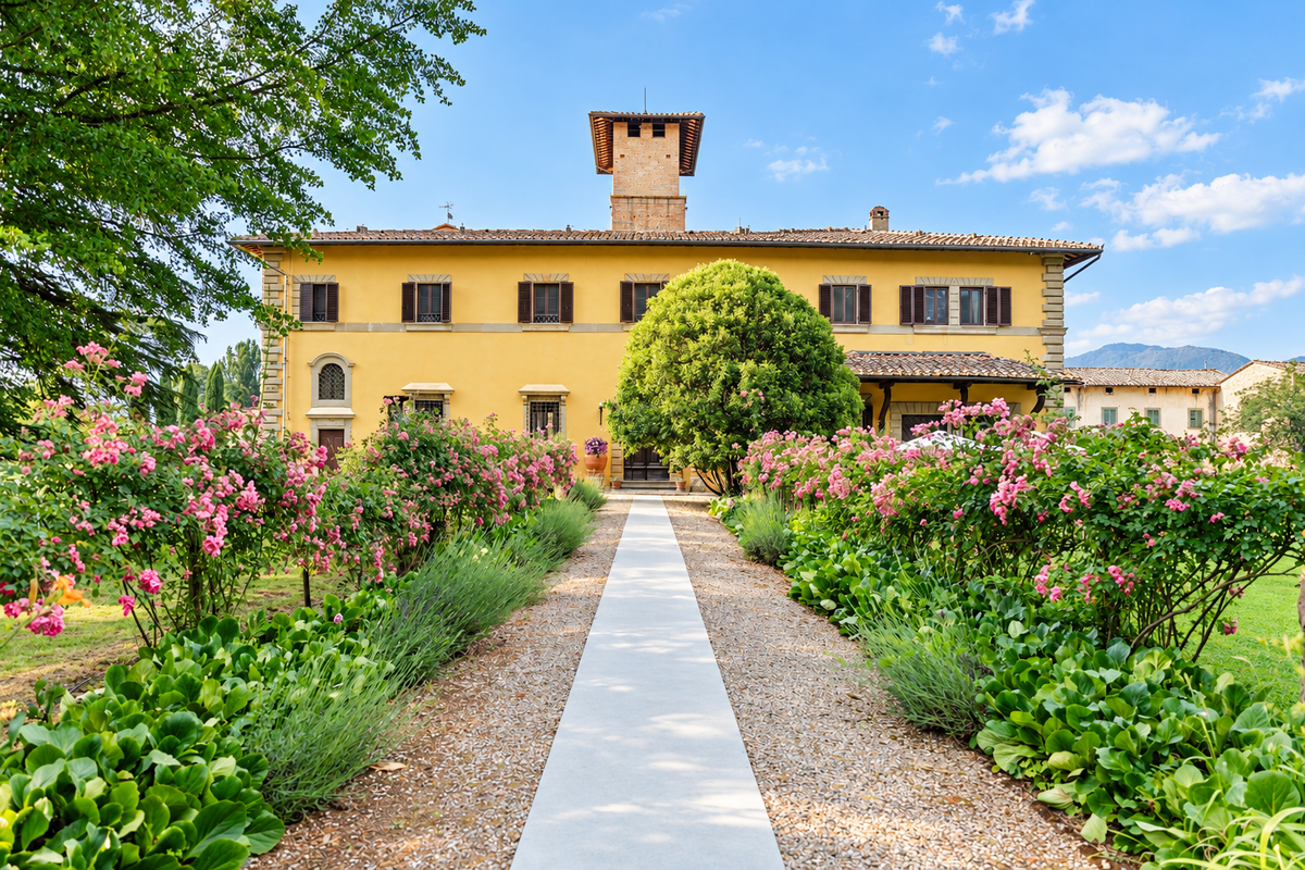 Castello del Monsignore's ochre facade and tower above a path lined with roses