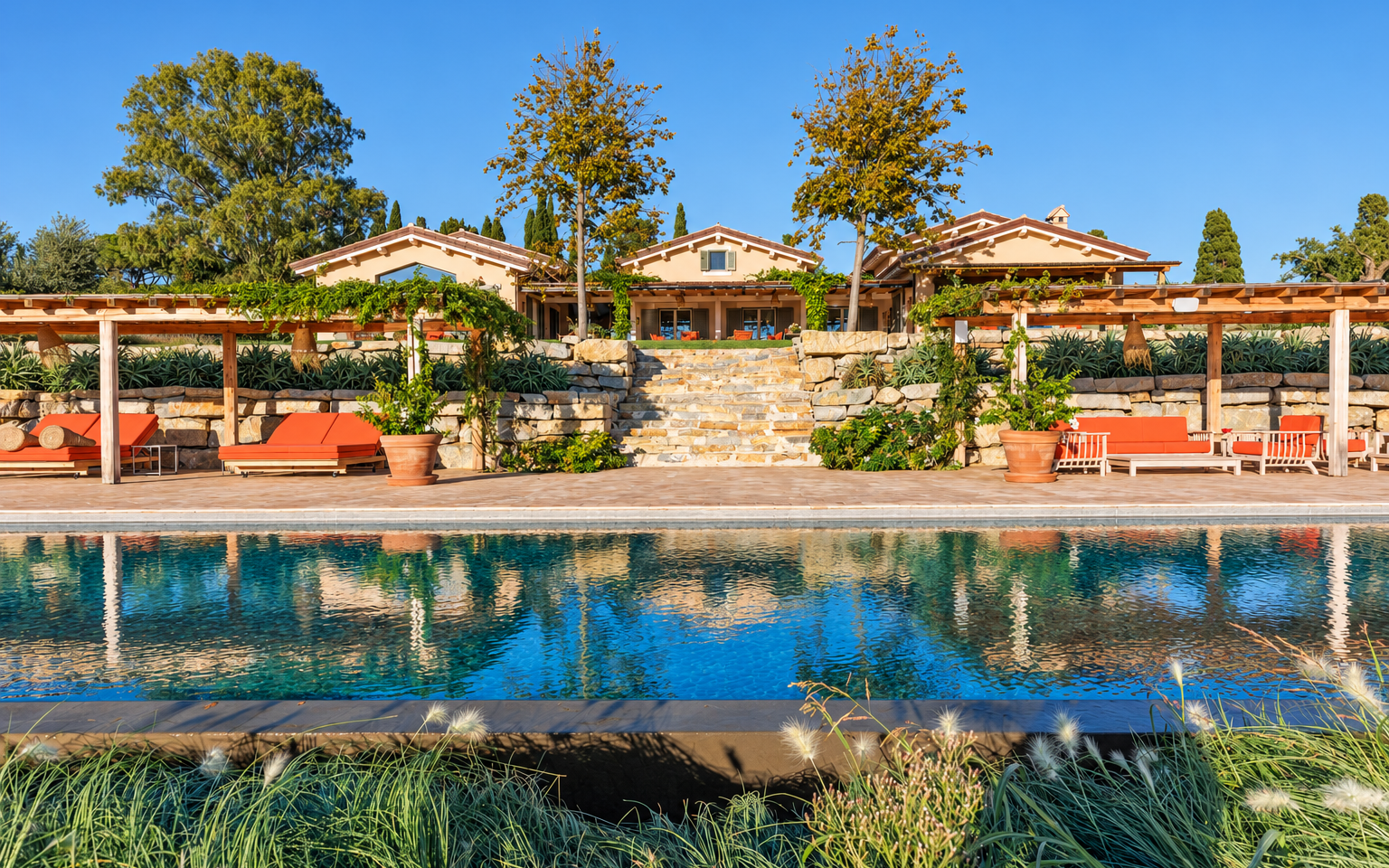 The villa reflected in the pool, behind stone walls and pergolas
