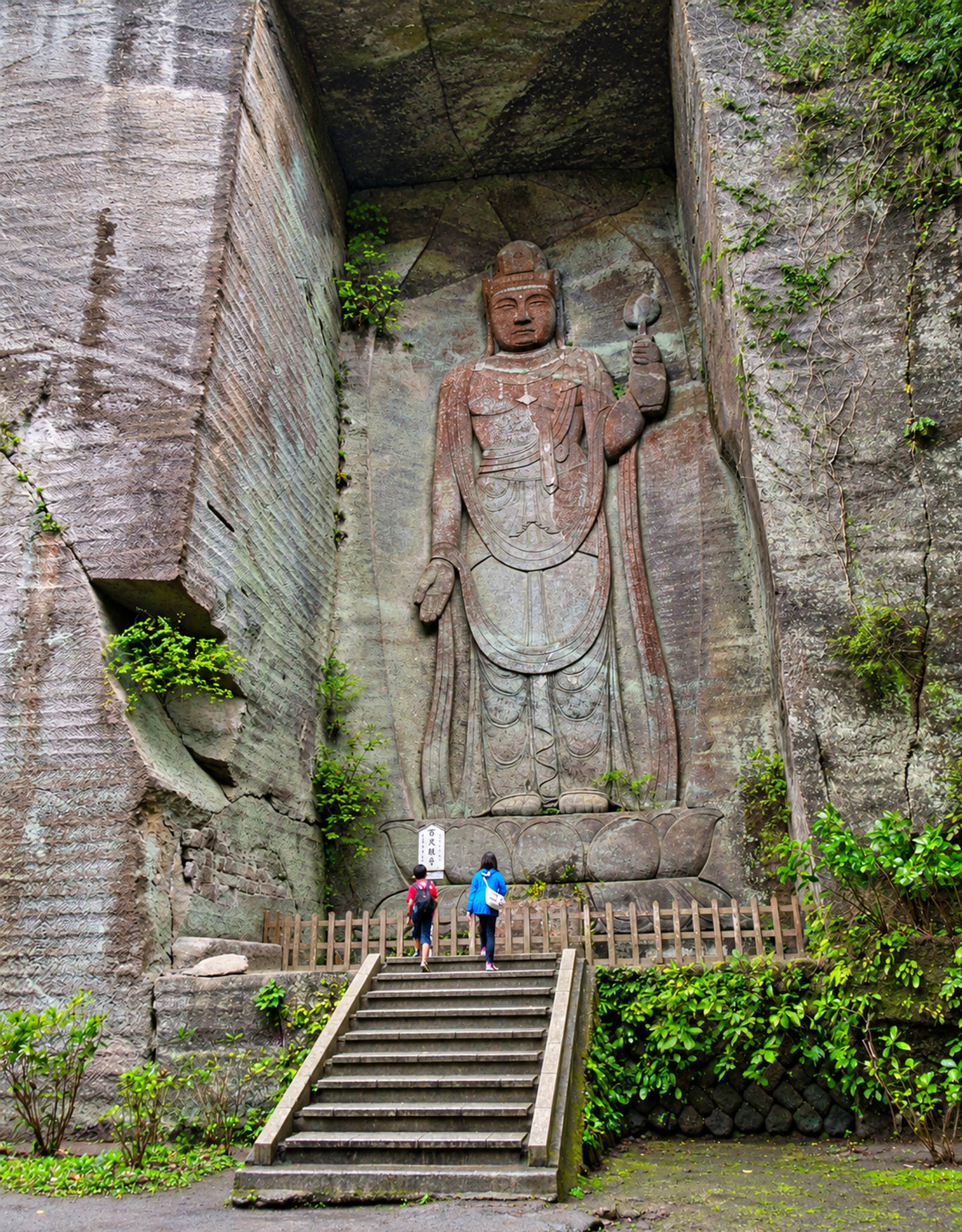 Grande statue bouddhique sculptée dans une paroi rocheuse, visiteurs au pied