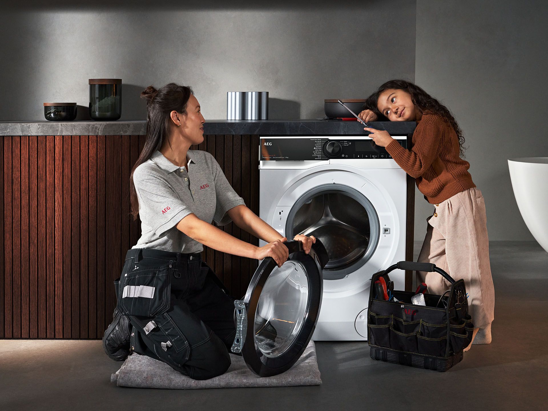 Service technician and child in front of washing machine being repaired