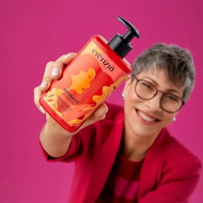 A woman holding up a bottle of Erenzia hair care