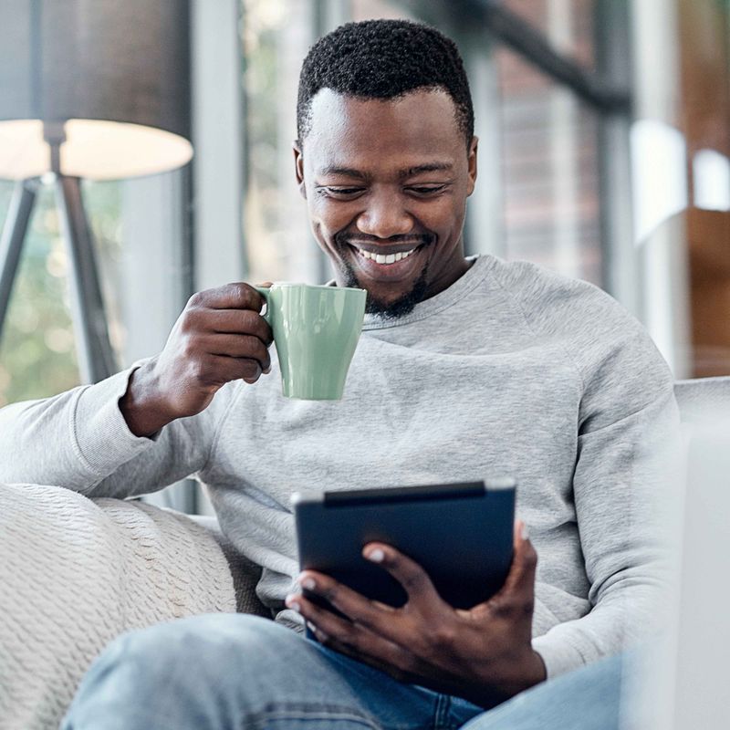Man Looking at iPad While Drinking Coffee on a Couch