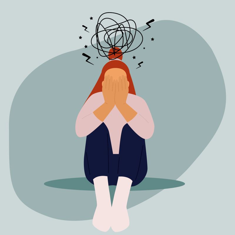 An illustration of a person, with a dejected body posture, sitting with swirls around their head and body to visualize the feeling of an anxiety attack.