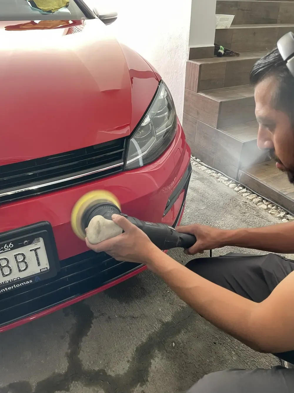 Detallador puliendo la cajuela de un Volkswagen Golf rojo en la cochera del cliente
