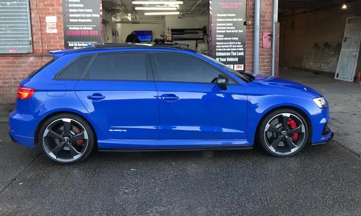 A blue Audi RS3 with gloss black roof bars and badges