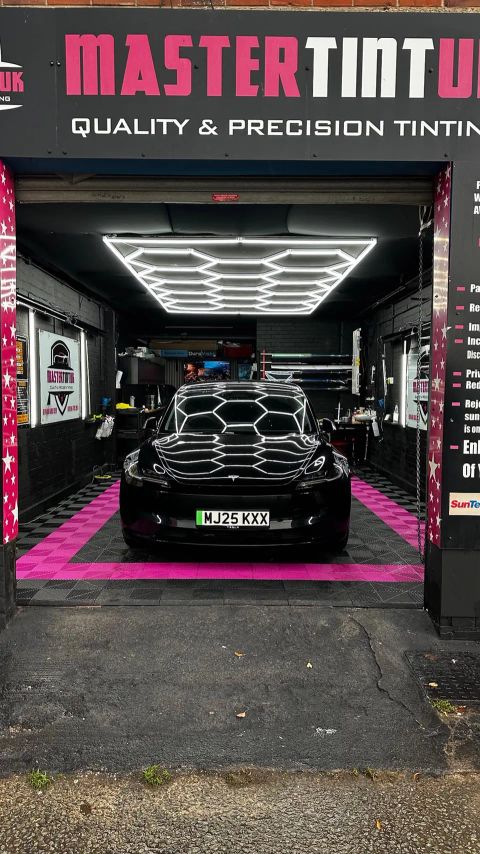 Black Tesla Model 3 in the bay at MasterTint UK, Weston Street, Bolton, seen from the street under the shop sign