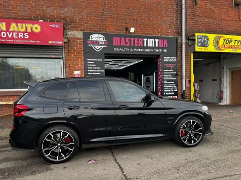 Black BMW X3 M with dark-tinted rear windows, side on, outside MasterTint UK, Weston Street, Bolton
