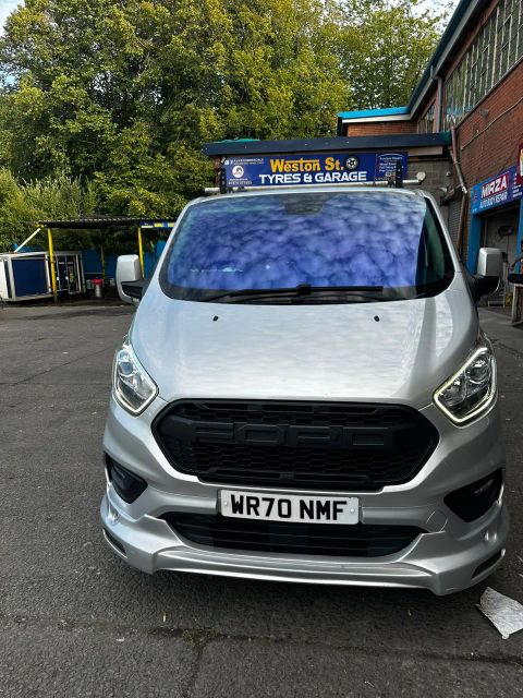 Silver Ford Transit Custom with a blue colour-shift windscreen film on Weston Street, Bolton