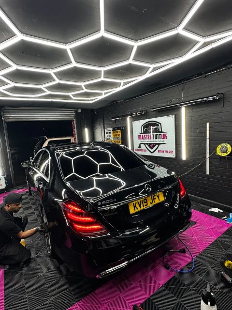 Black Mercedes S400d with dark-tinted rear windows and rear screen in the MasterTint UK bay, Weston Street, Bolton, a fitter finishing the wheels