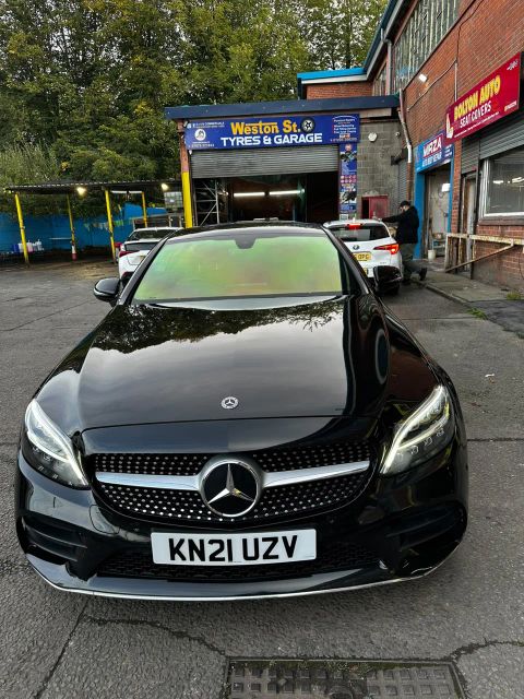 Black Mercedes C220d Coupe with a green-gold colour-shift windscreen film on Weston Street, Bolton