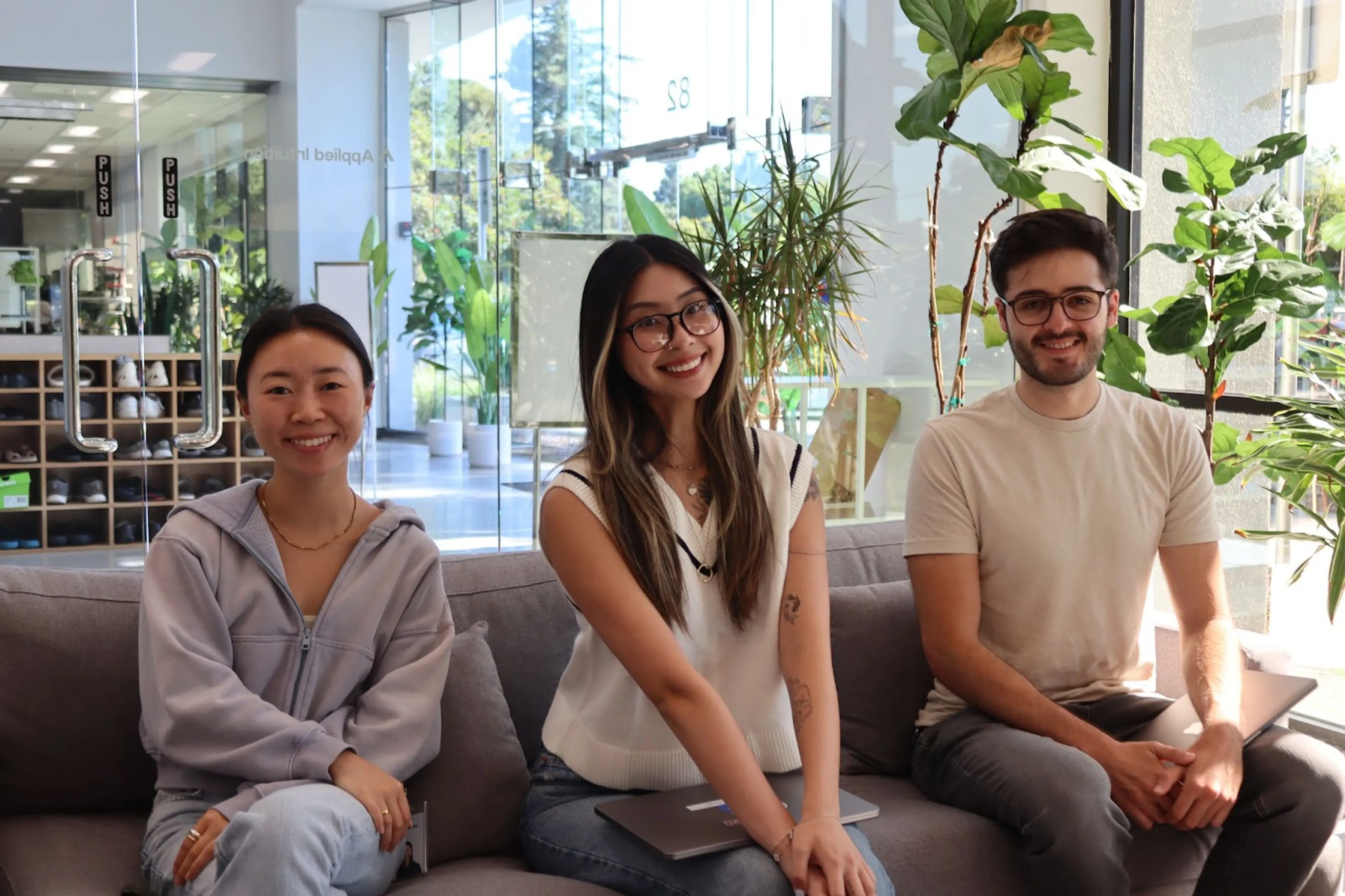Three employees seated on a sofa in the lobby of Applied Intuition, from left to right: Jasmine Wu, Sonam Huang, and Richie Goulazian.