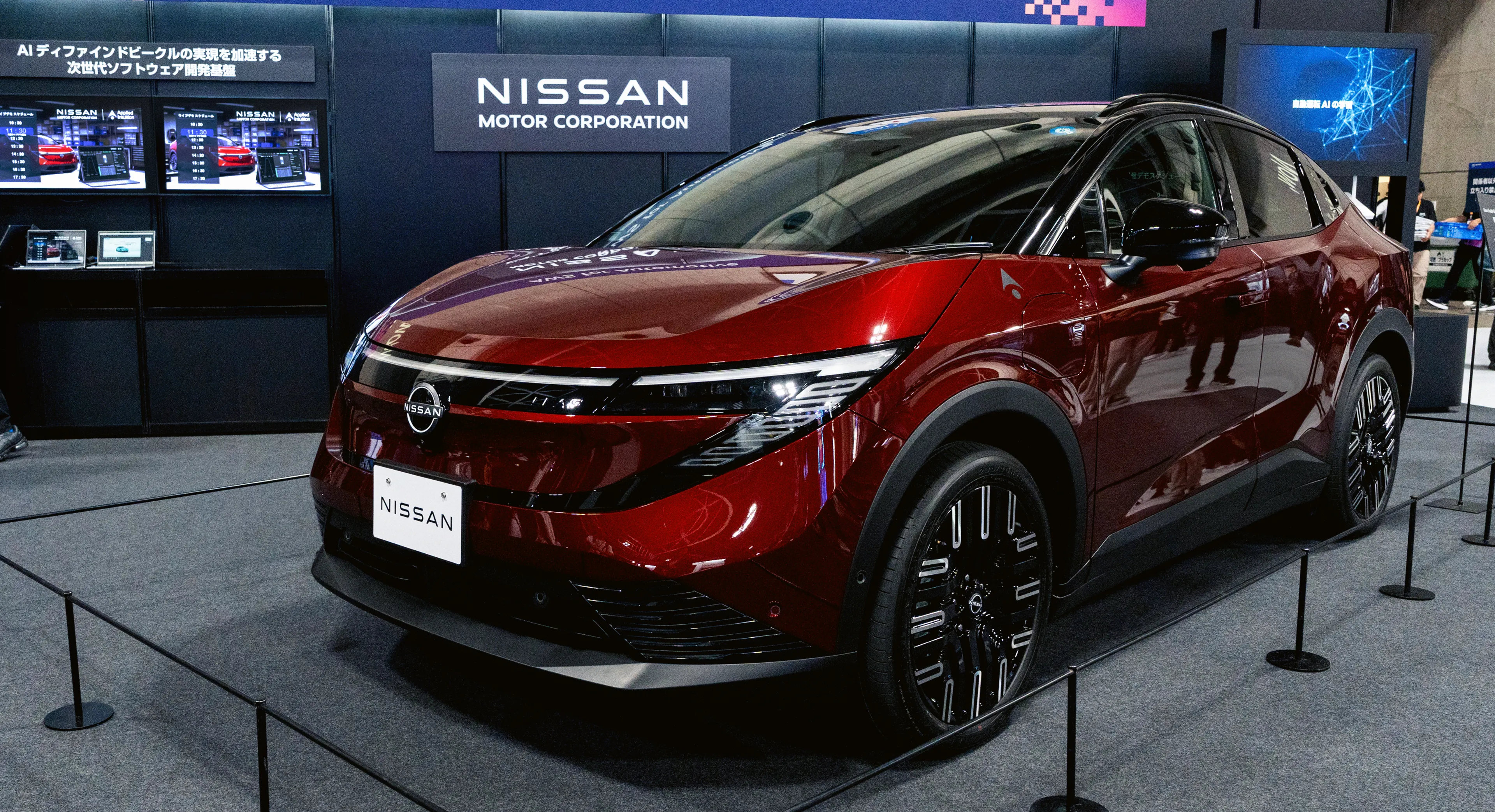 A red Nissan vehicle on display at an AWS for Automotive exhibition booth, with Japanese-language signage and product displays visible in the background
