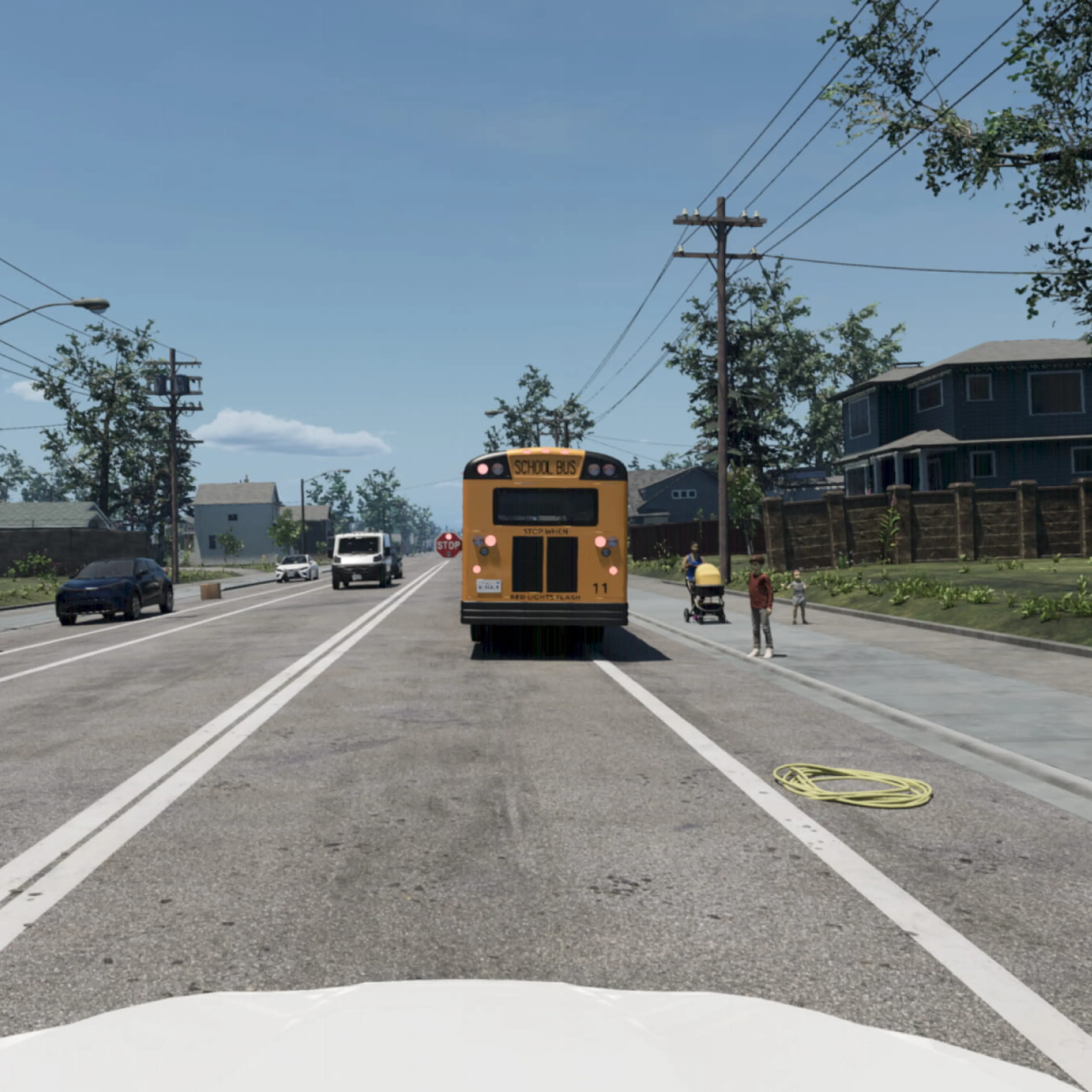A driver's-eye view of a suburban road with a stopped yellow school bus ahead, its red stop sign extended, as pedestrians stand on the sidewalk to the right.