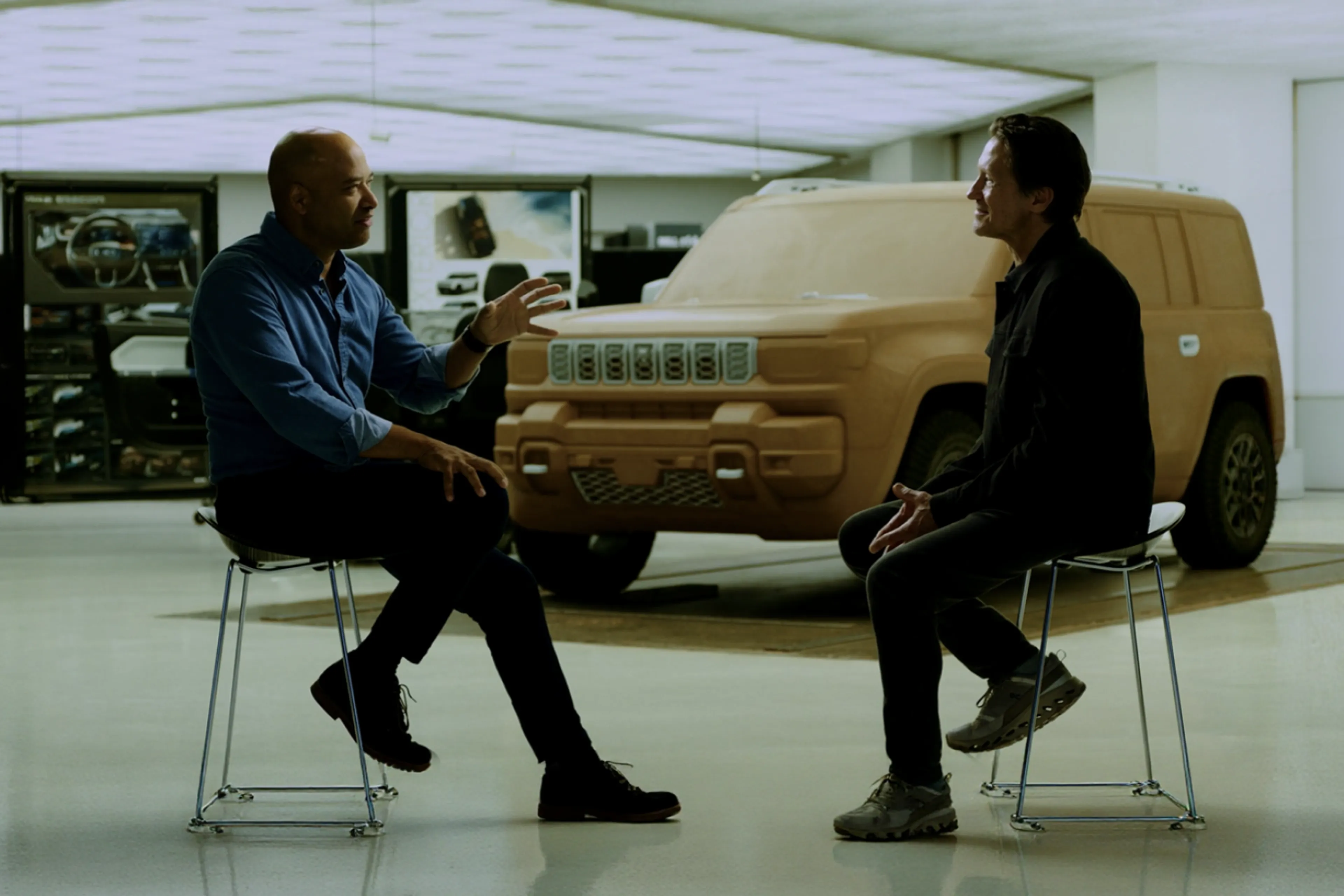 Ralph Gilles and Karl Heiselman talk in a Stellantis design studio in front of a full-size clay model of a Jeep SUV.