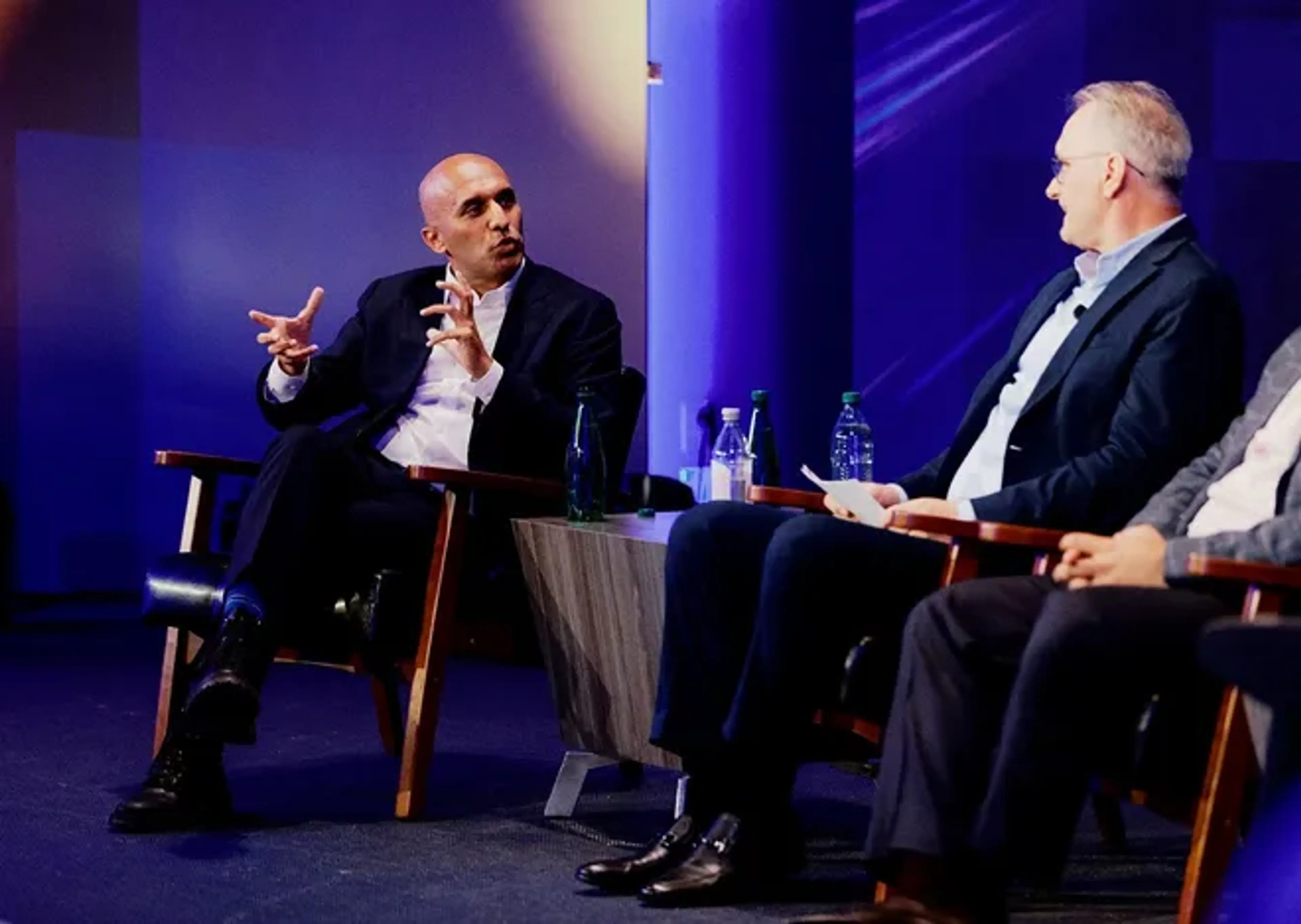 Applied Intuition CEO Qasar Younis gestures while speaking with Stellantis CTO Ned Curic during a panel discussion at Stellantis' investor day in Auburn Hills.