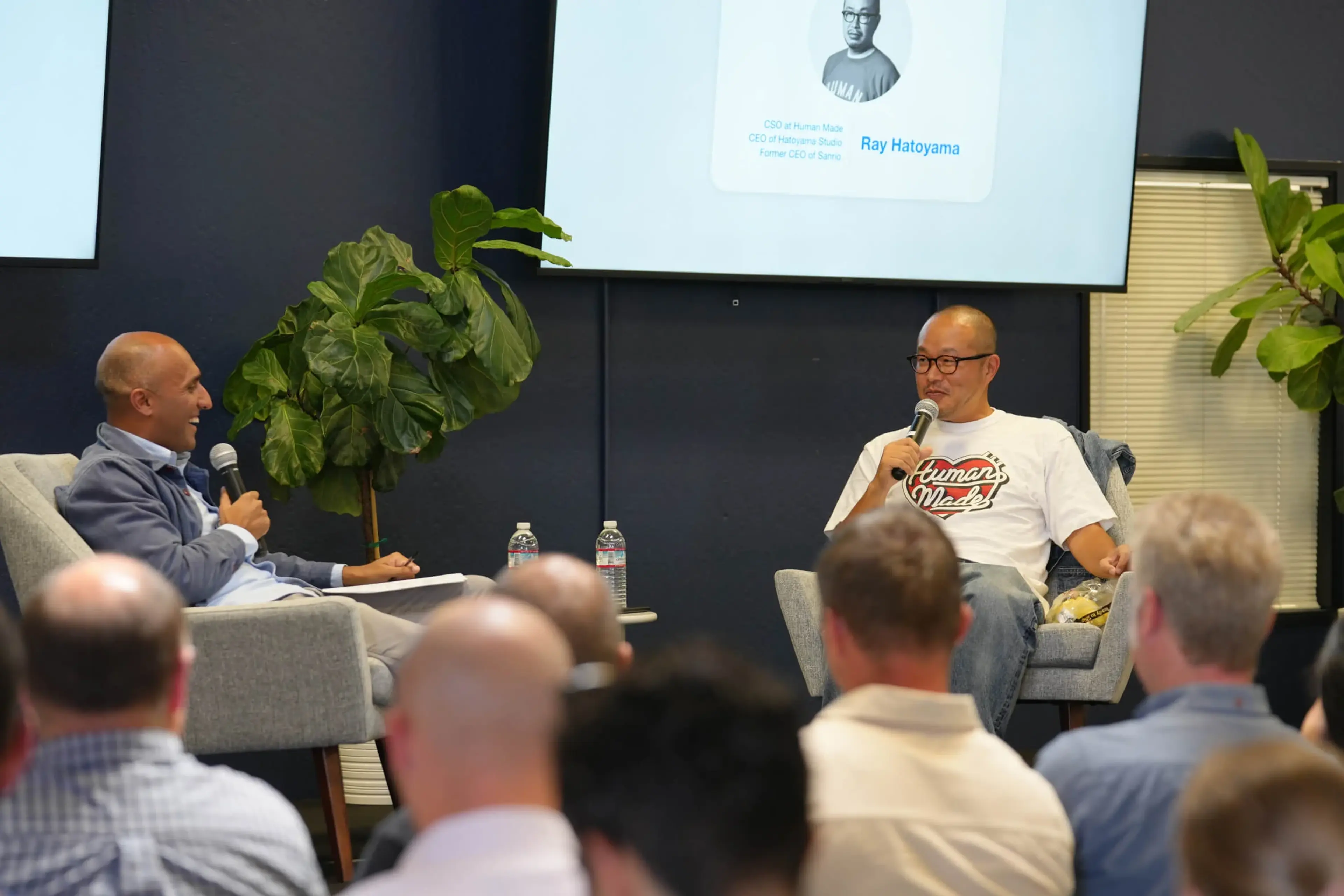 Qasar Younis in conversation with Ray Hatoyama, both holding microphones while speaking to an audience