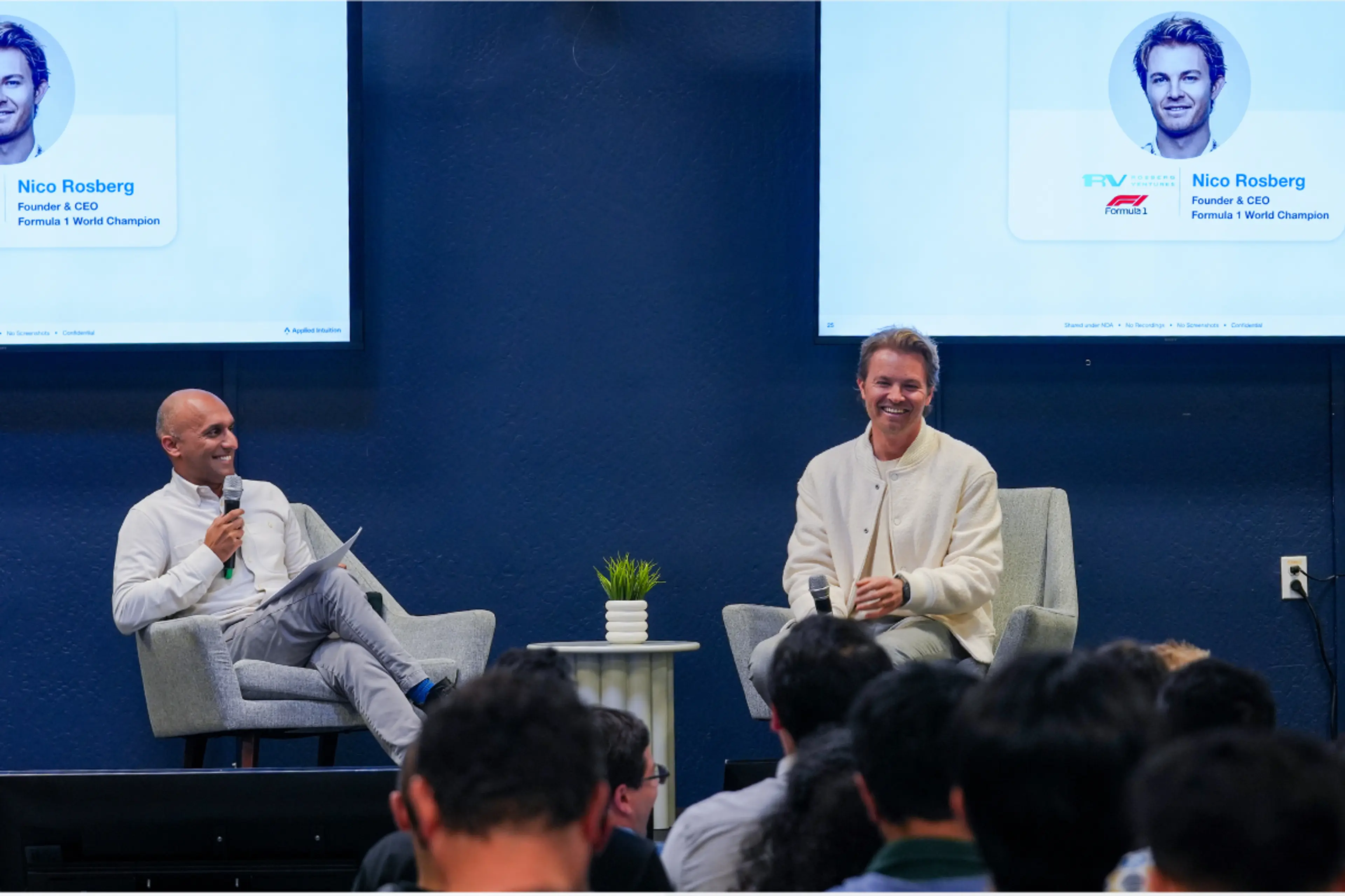 Qasar Younis is seated left and Nico Rosberg is seated right on a stage facing an audience