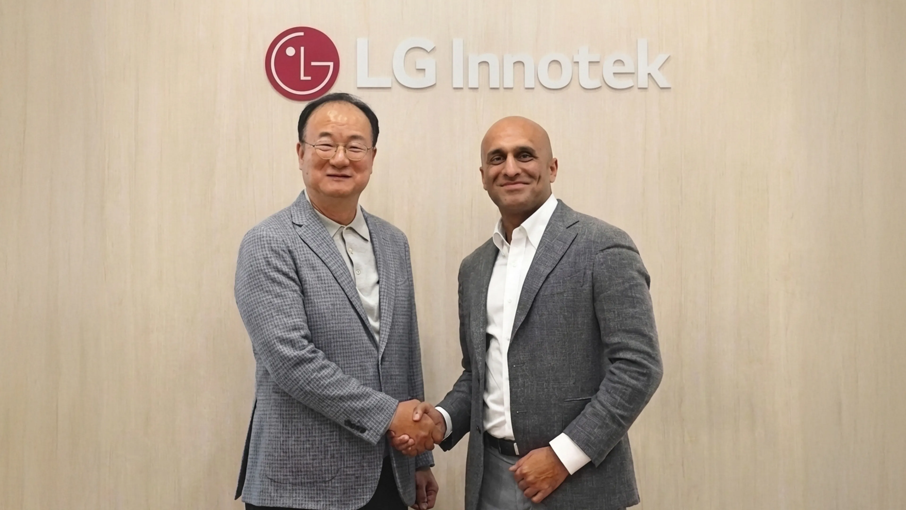 Two men in grey blazers shake hands in front of an LG Innotek logo and wordmark on a white wall